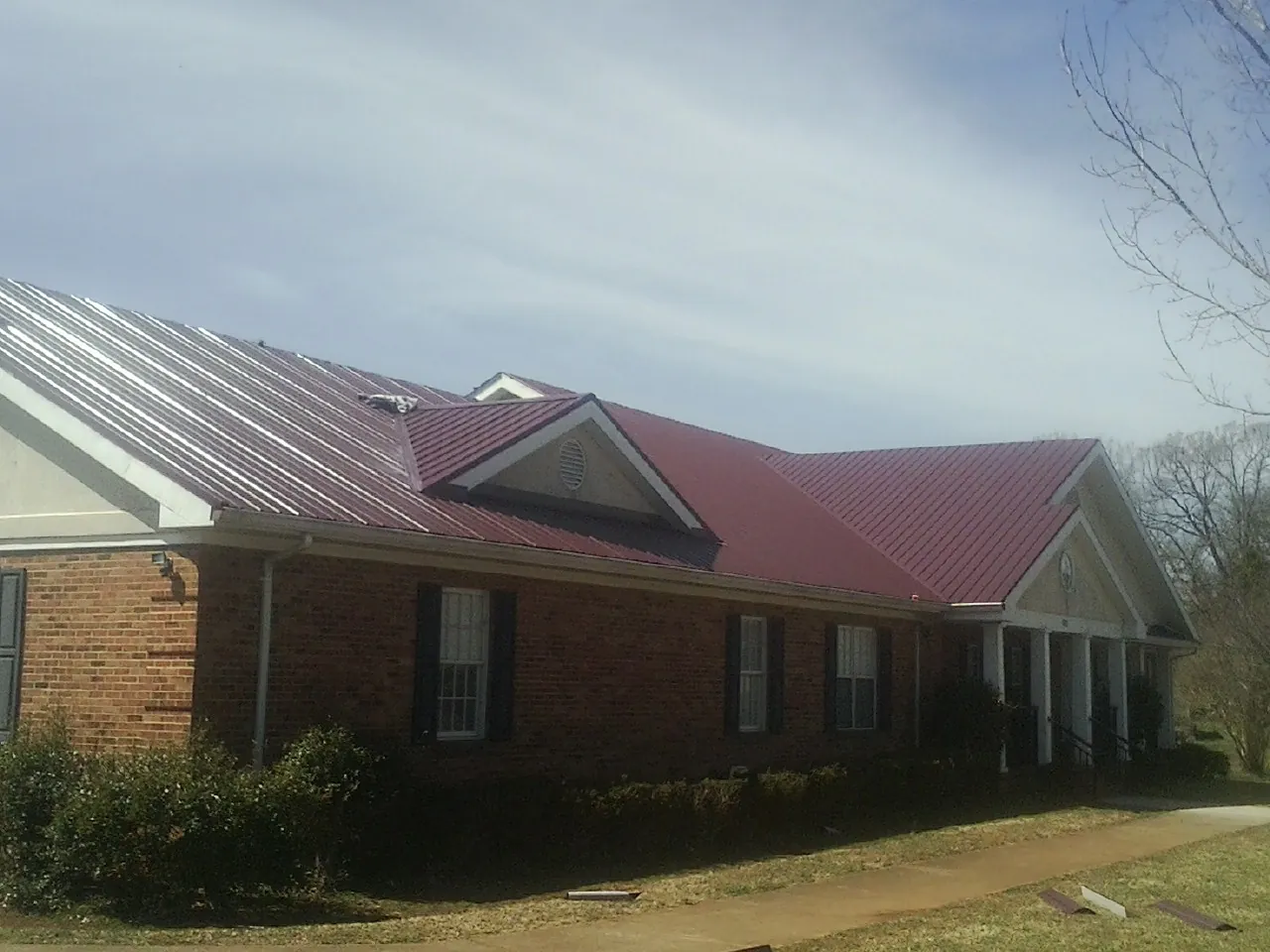 Red metal roof with gabled entries on a long brick building, from a Hail Damage Roof Repair job in Minooka