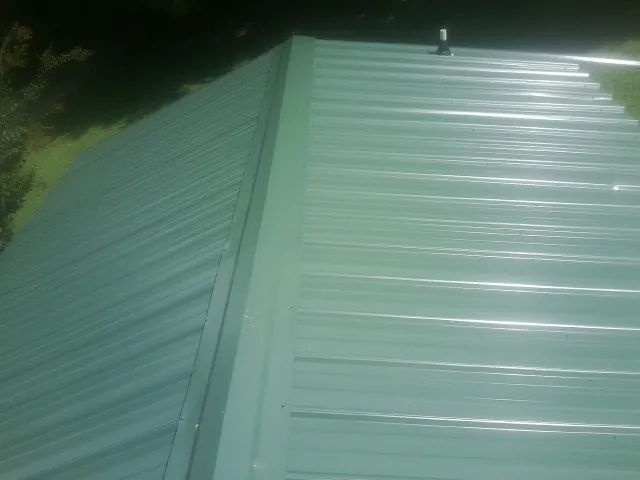 New green metal panels meeting at the ridge of a roof — Flat Roof Repair work by our crew in Minooka