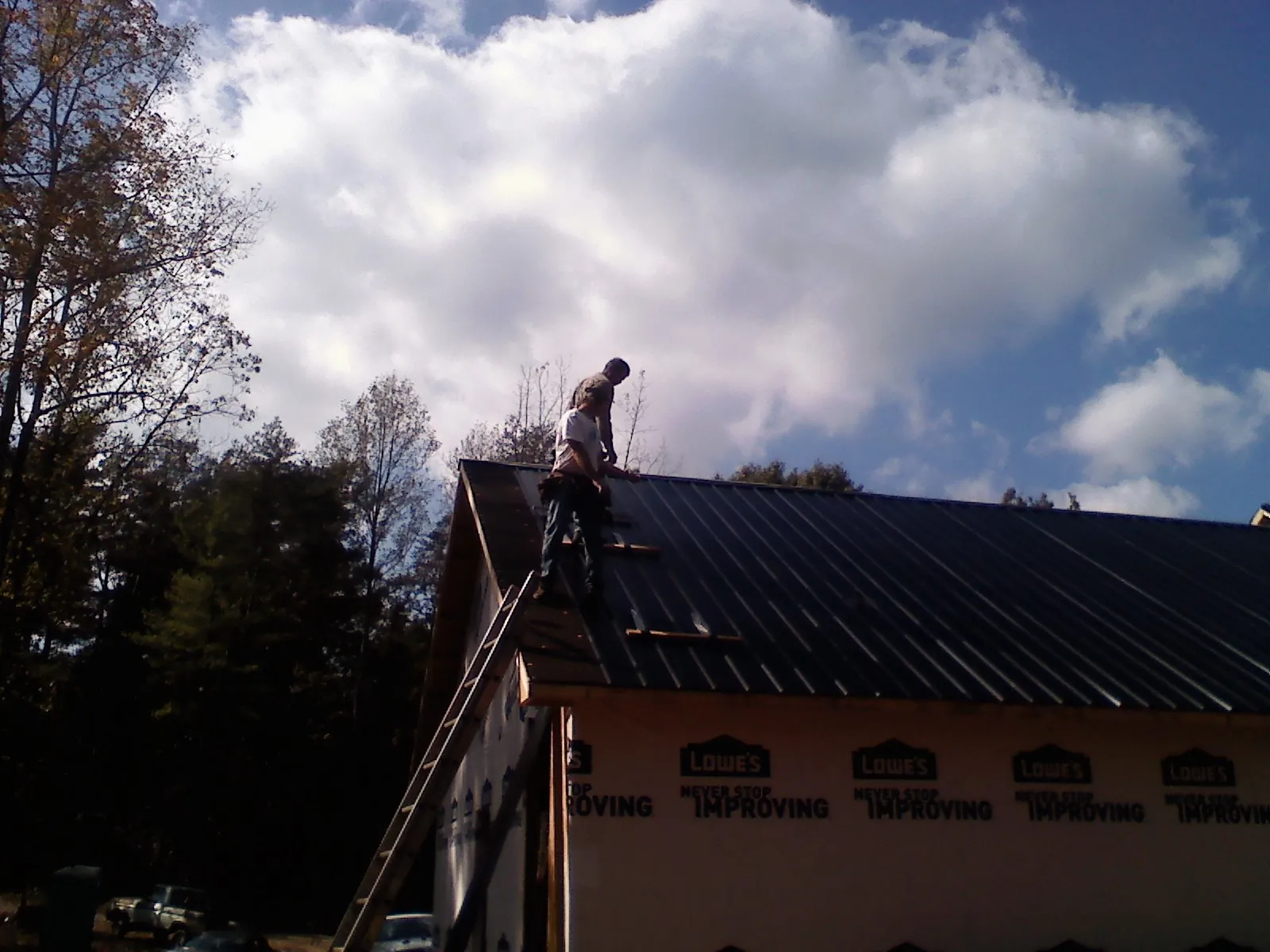 Roofer fastening dark metal panels high against a cloudy sky, from a Roof Inspection job in Minooka