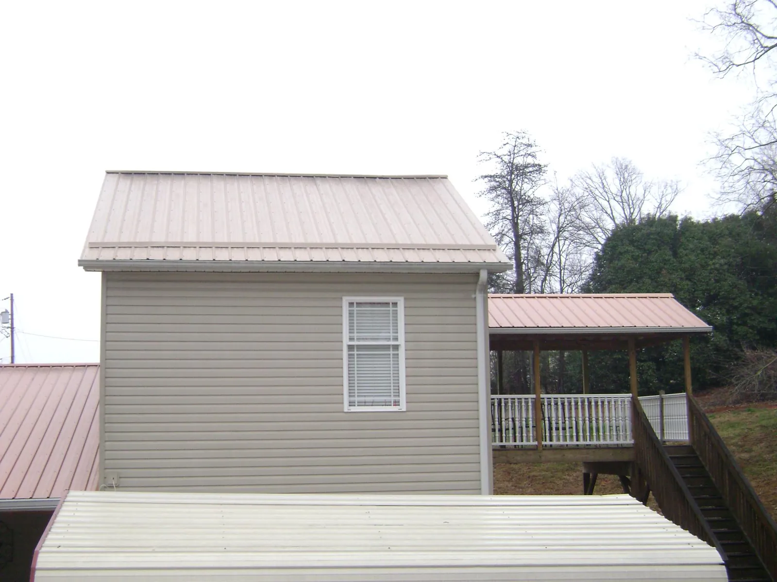 Tan metal roofs on a two story addition and attached porch, from a Roof Replacement job in Minooka